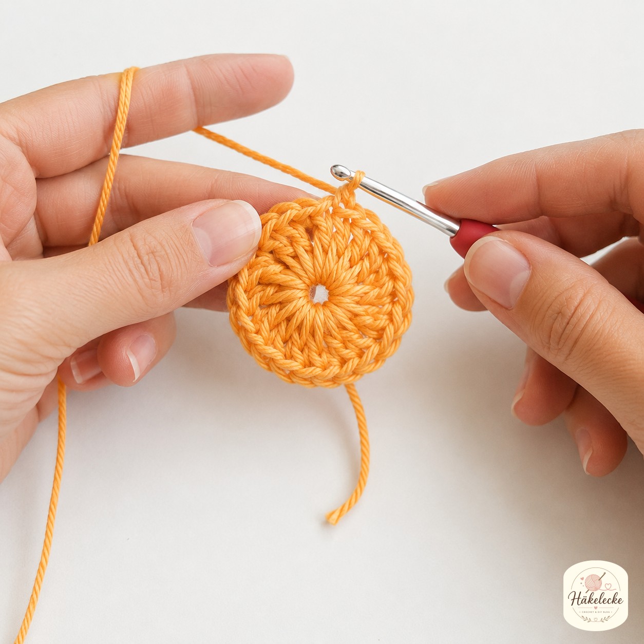 Die erste Runde der African Flower Granny Square Anleitung entsteht als orange Blüte im magischen Ring