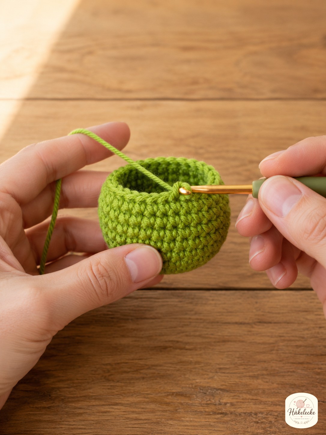 Hände häkeln eine kleine grüne Kugel in festen Maschen für den Kopf des Grinch Amigurumi mit Schal
