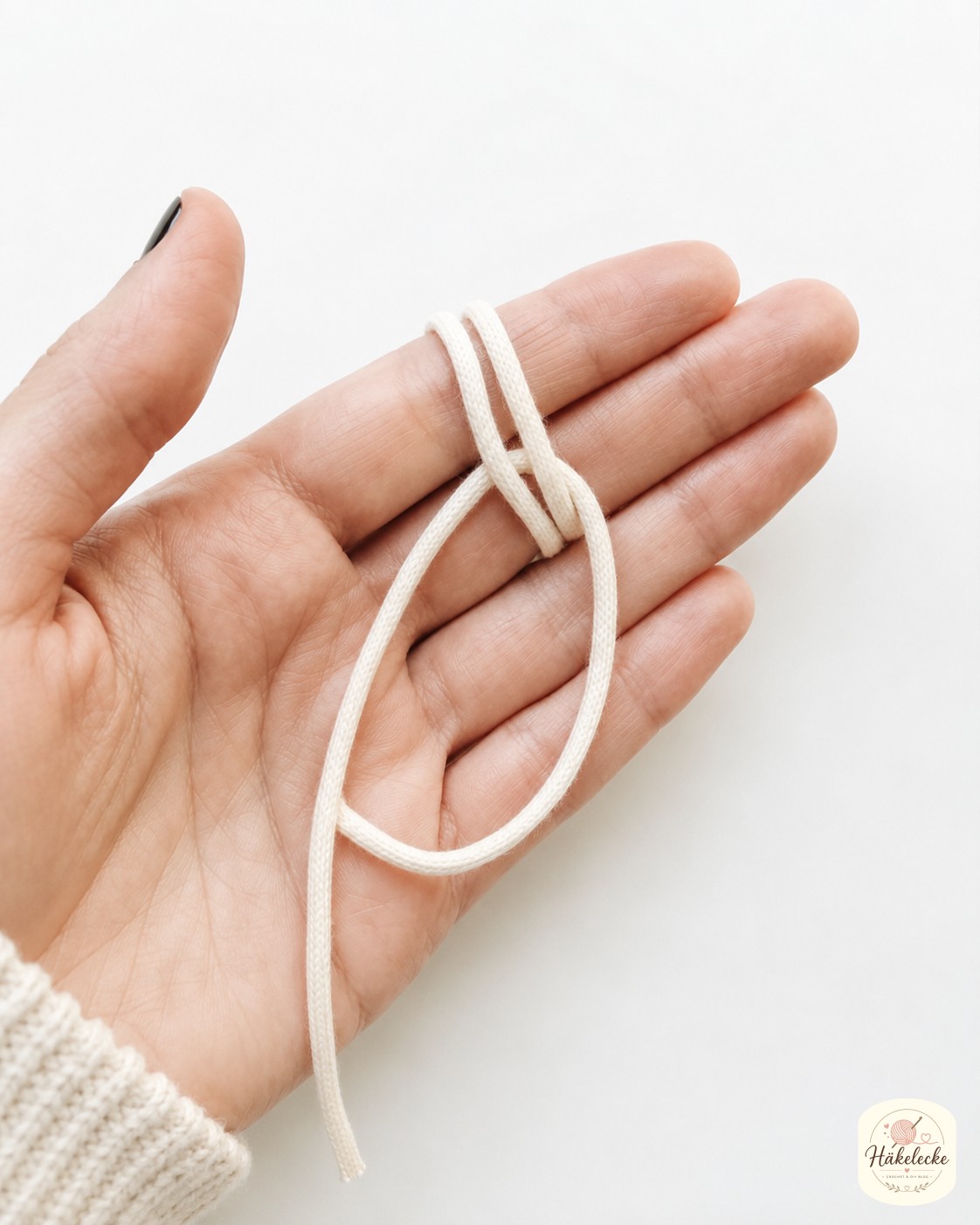 Die Hand wickelt die Kordel zweimal um die Finger, der erste Schritt beim magischen Ring häkeln
