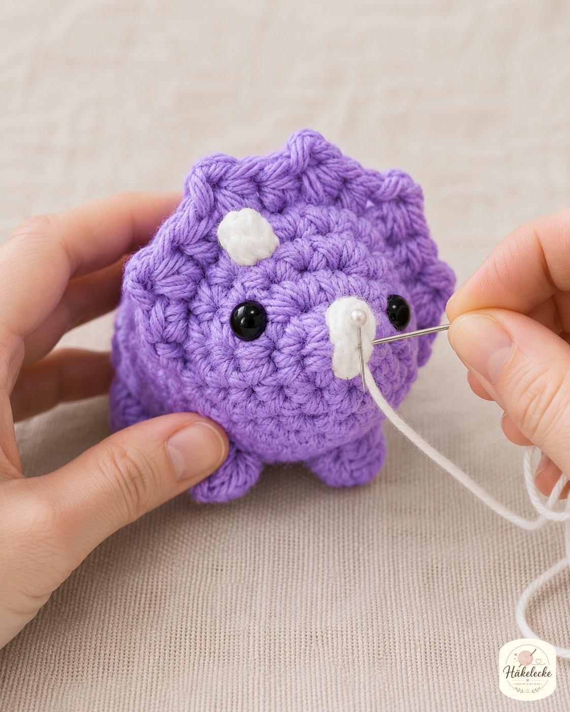 Schwarze Sicherheitsaugen und weiße Hornflecken geben dem Mini Triceratops Amigurumi seinen Blick.