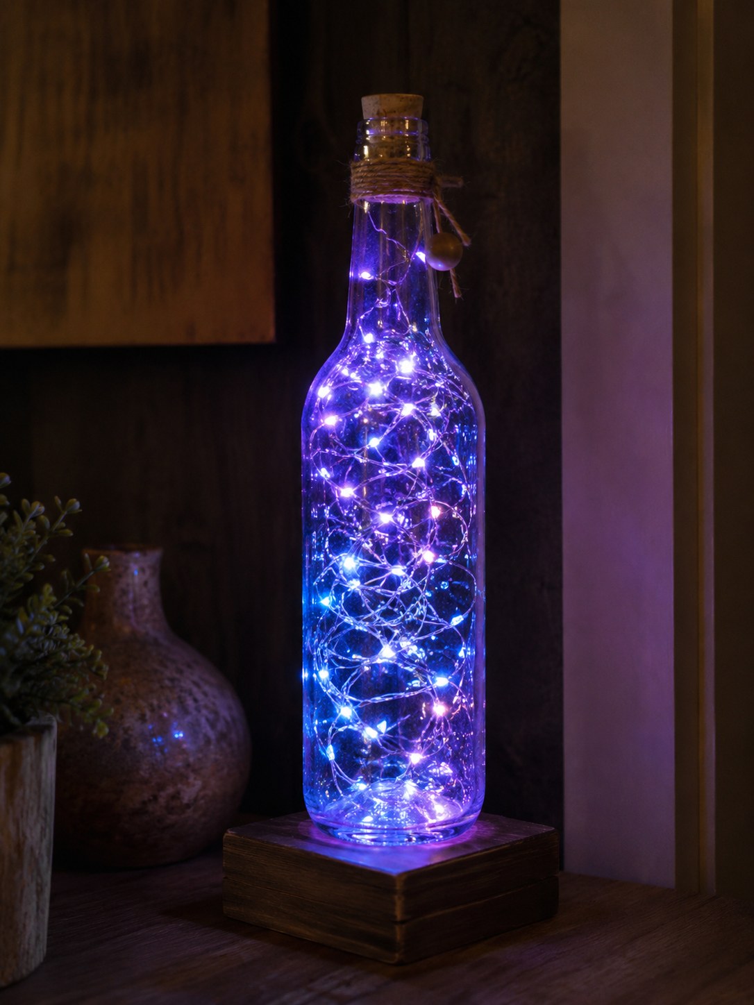 Eine Glasflasche mit warmer Lichterkette im Inneren leuchtet als stimmungsvolle Upcycling-Lampe auf Holzsockel.