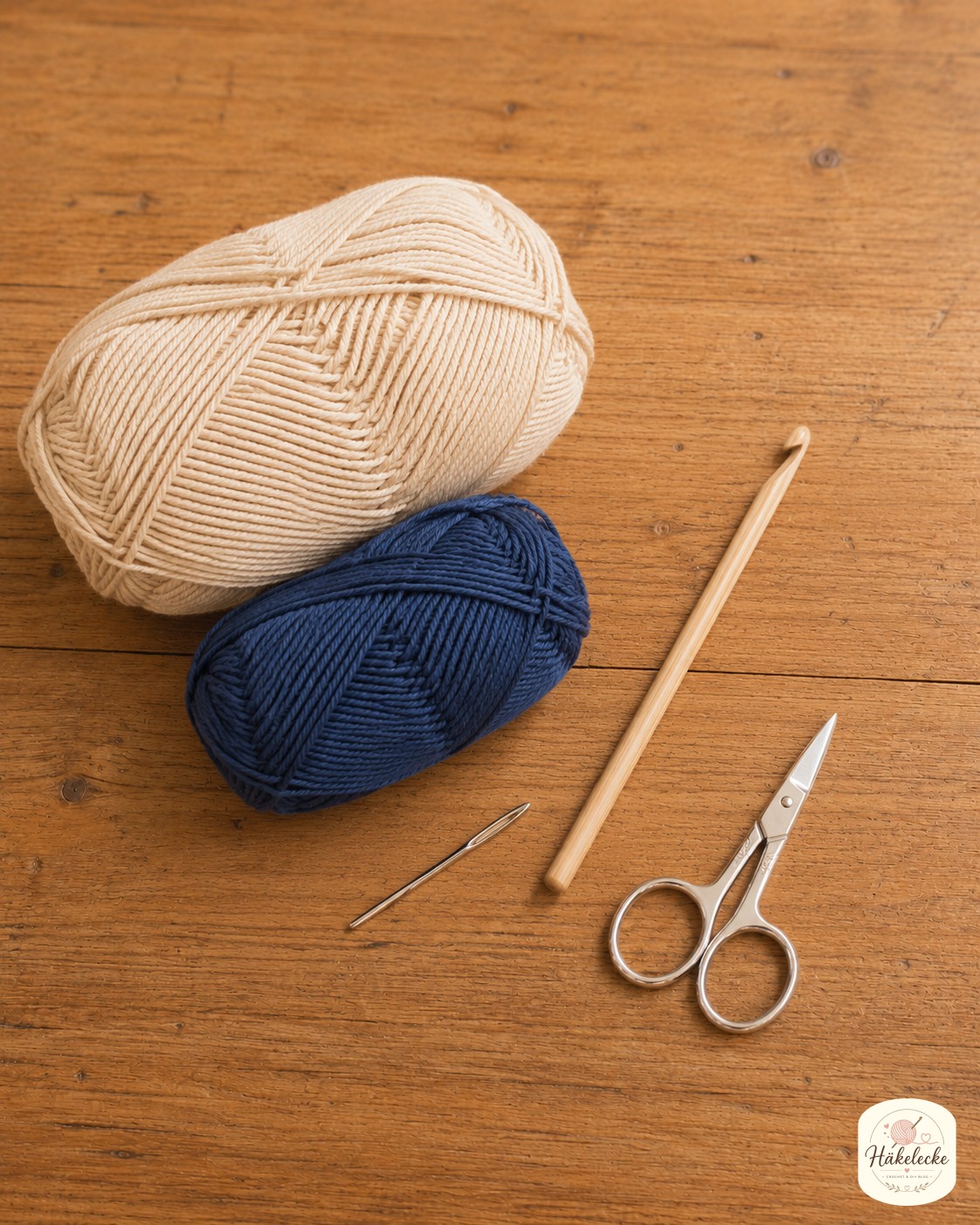 Baumwollgarn in Beige und Navy liegt mit Häkelnadel und Maßband bereit zum Topflappen häkeln.